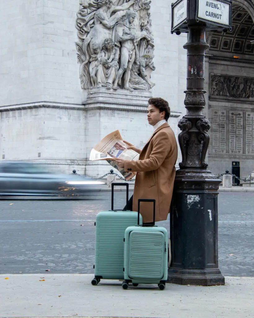 Man with suitcases reading a newspaper by the Arc de Triomphe in Paris