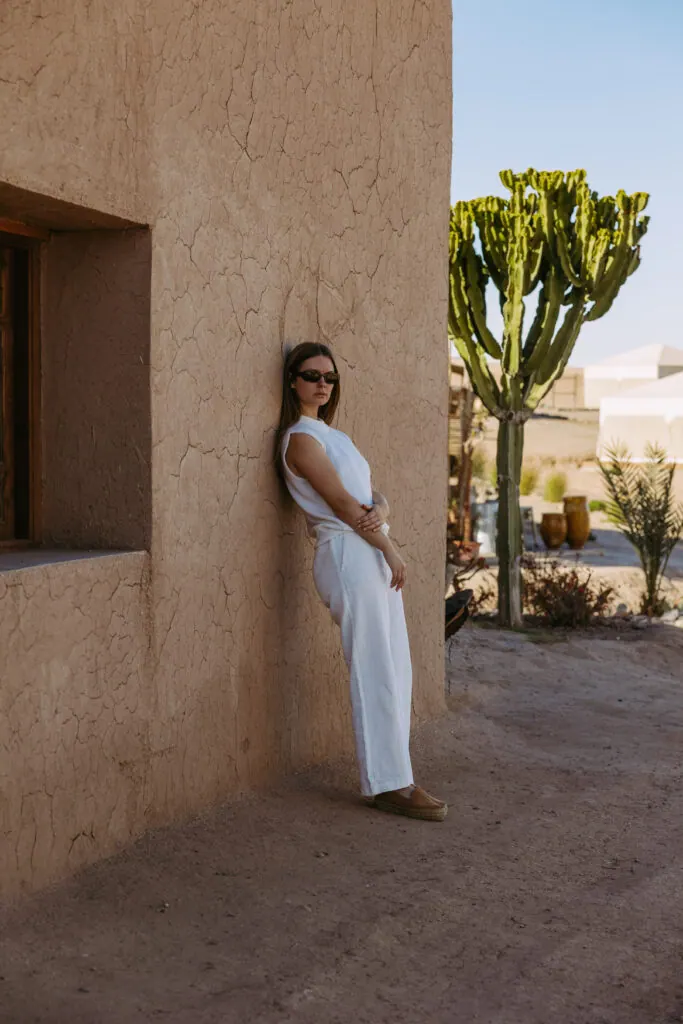 Woman in white leaning against a sunlit wall in Morocco
